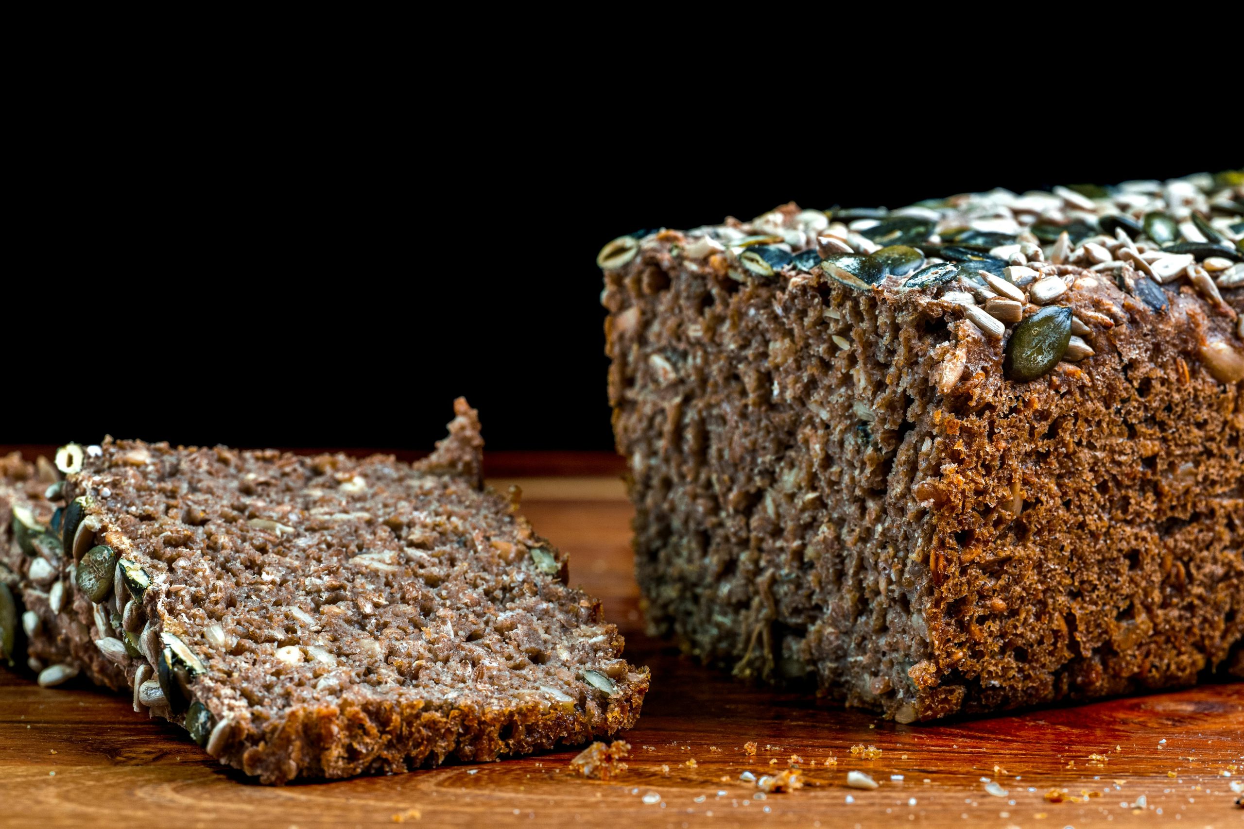 Gros plan de pain de seigle complet tranché garni de graines sur une surface en bois.