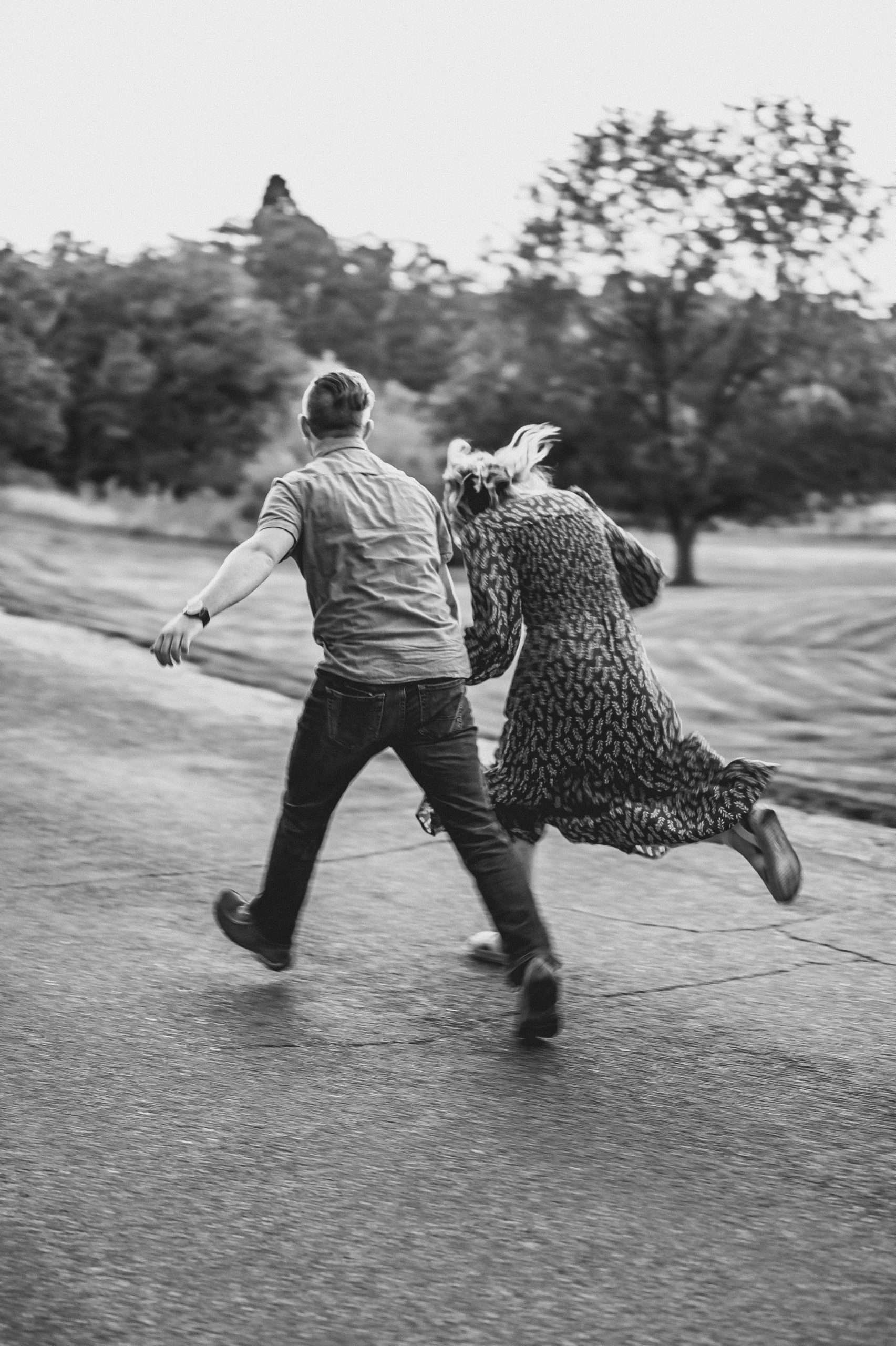 A joyful black and white image of a couple running together on a road, capturing dynamic motion and fun. Image en noir et blanc joyeuse d'un couple courant ensemble sur une route, capturant un mouvement dynamique et du plaisir.