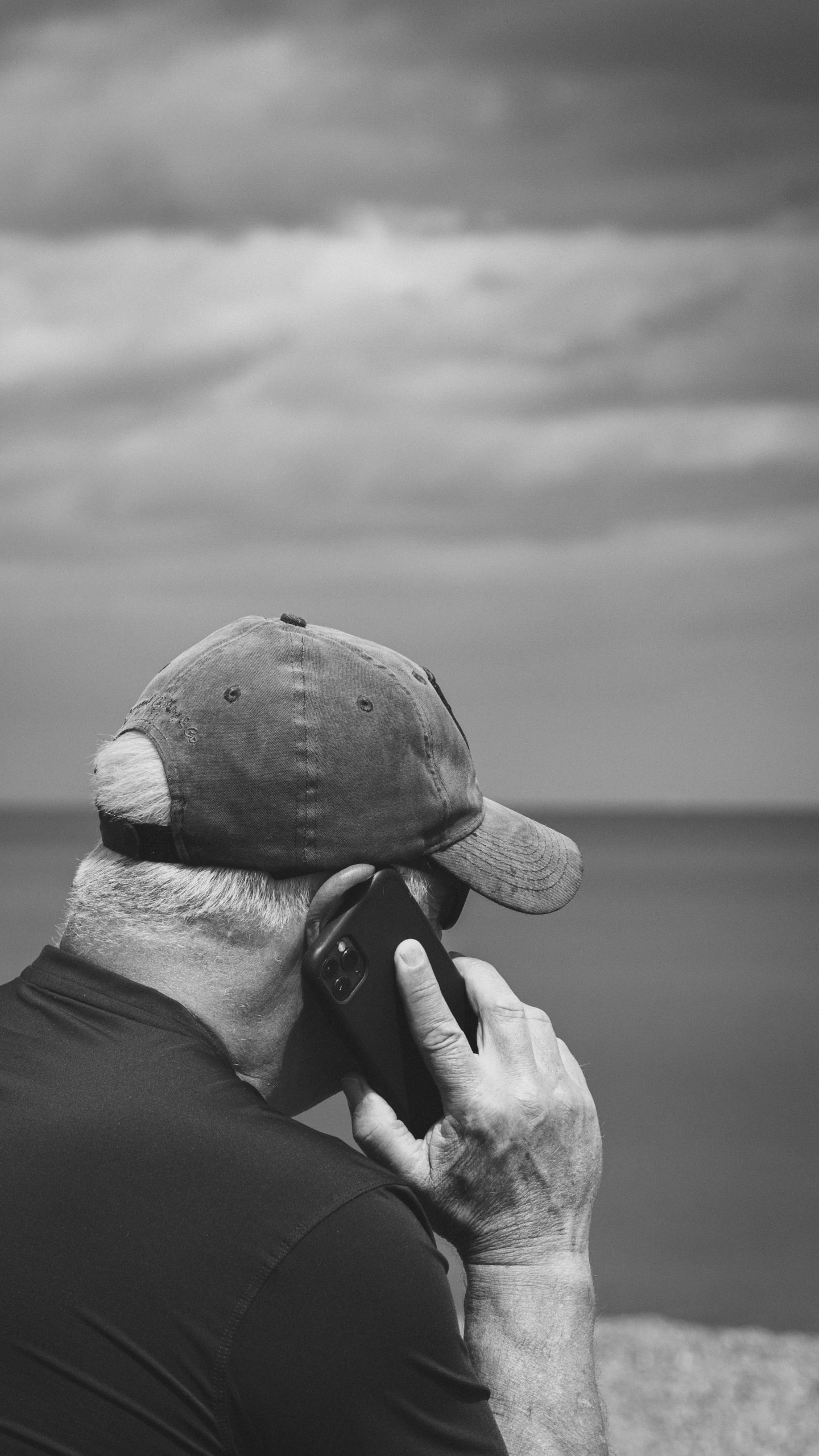 Homme adulte en noir et blanc passant un appel téléphonique près de la mer.