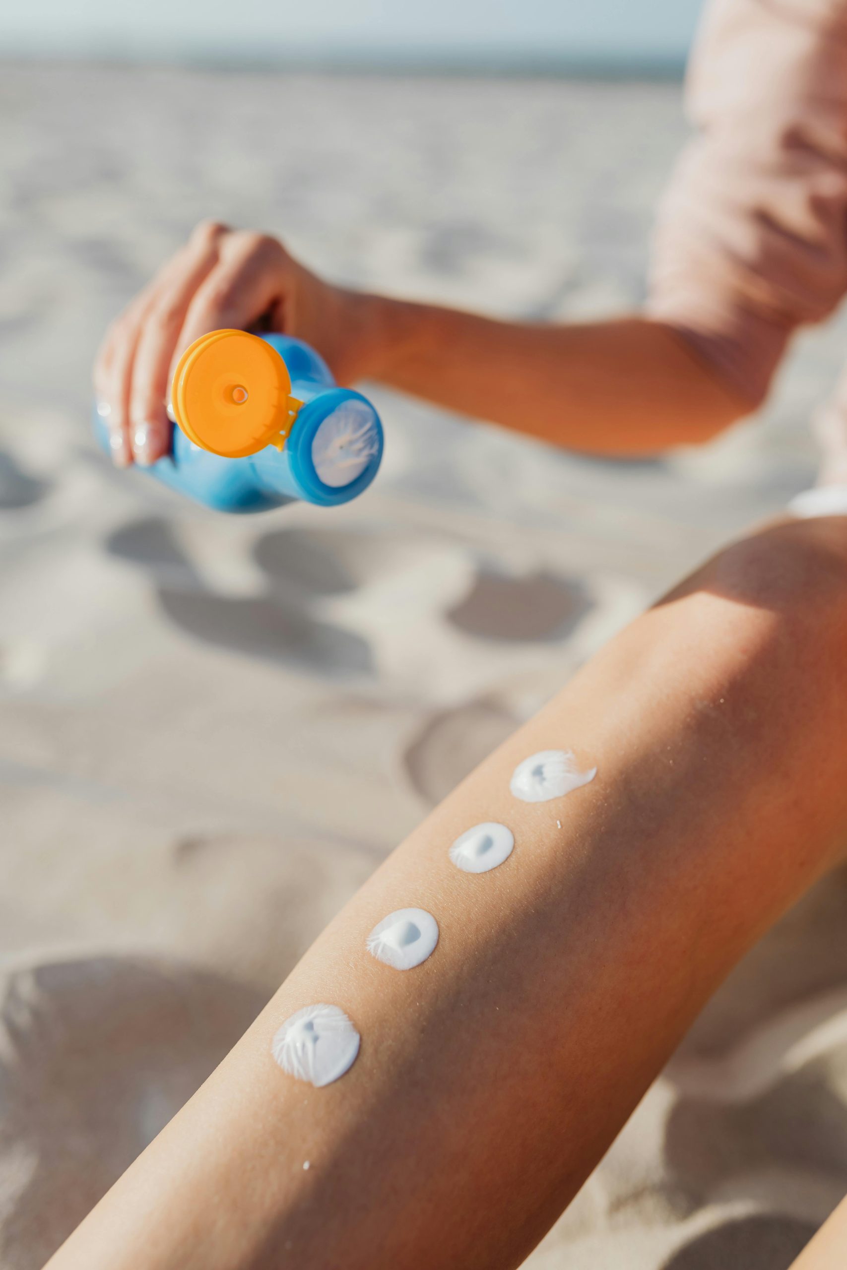 Femme appliquant de la crème solaire sur sa jambe à la plage. Routine de soins de la peau en été pour une protection solaire en extérieur.