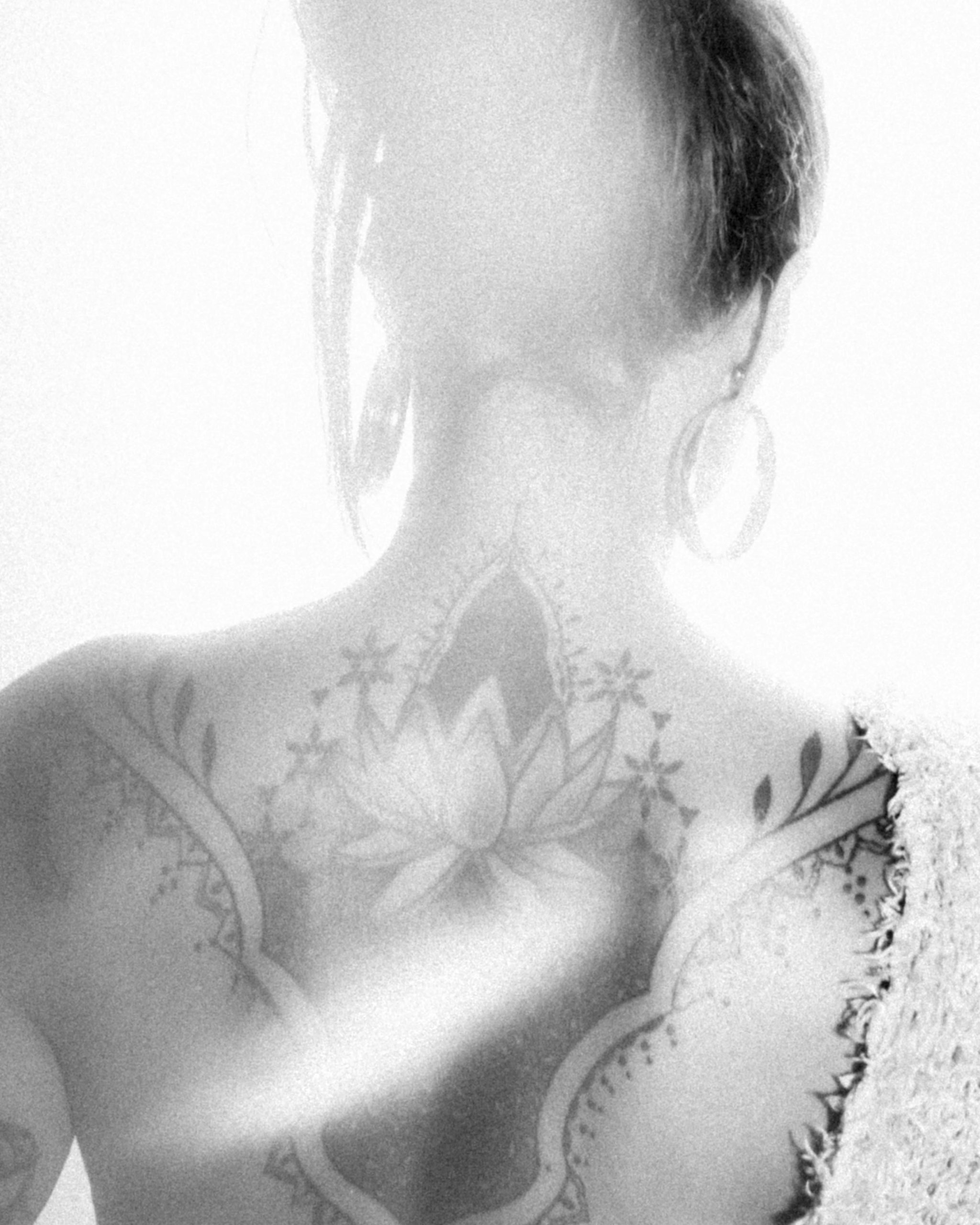 Black and white photograph showcasing a detailed tattoo on a woman's back under ethereal lighting. Photographie en noir et blanc mettant en valeur un tatouage détaillé sur le dos d'une femme sous un éclairage éthéré.