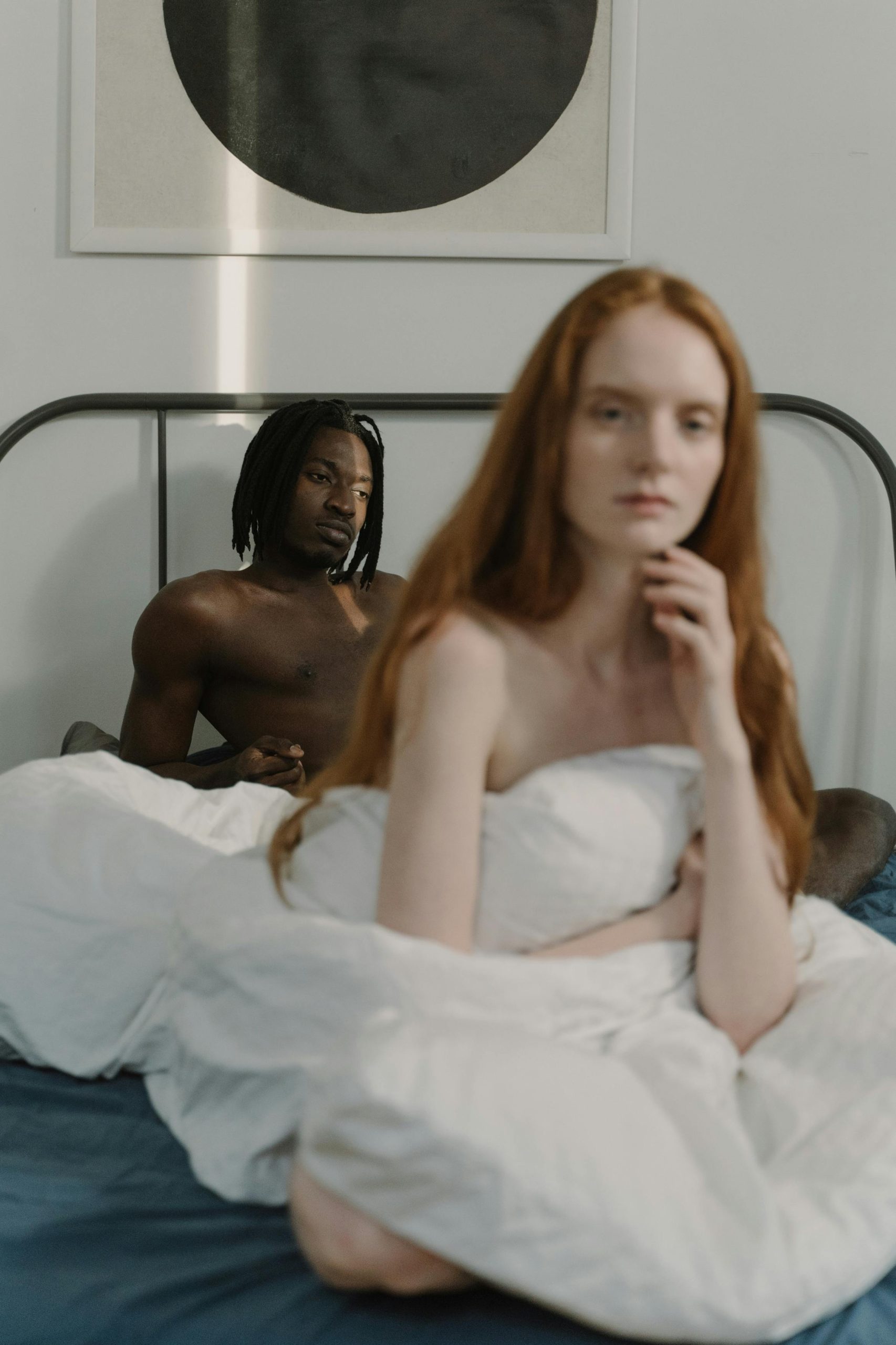A thoughtful couple sitting together in a minimalist bedroom, evoking connection and intimacy. Un couple réfléchi assis ensemble dans une chambre minimaliste, évoquant la connexion et l'intimité.
