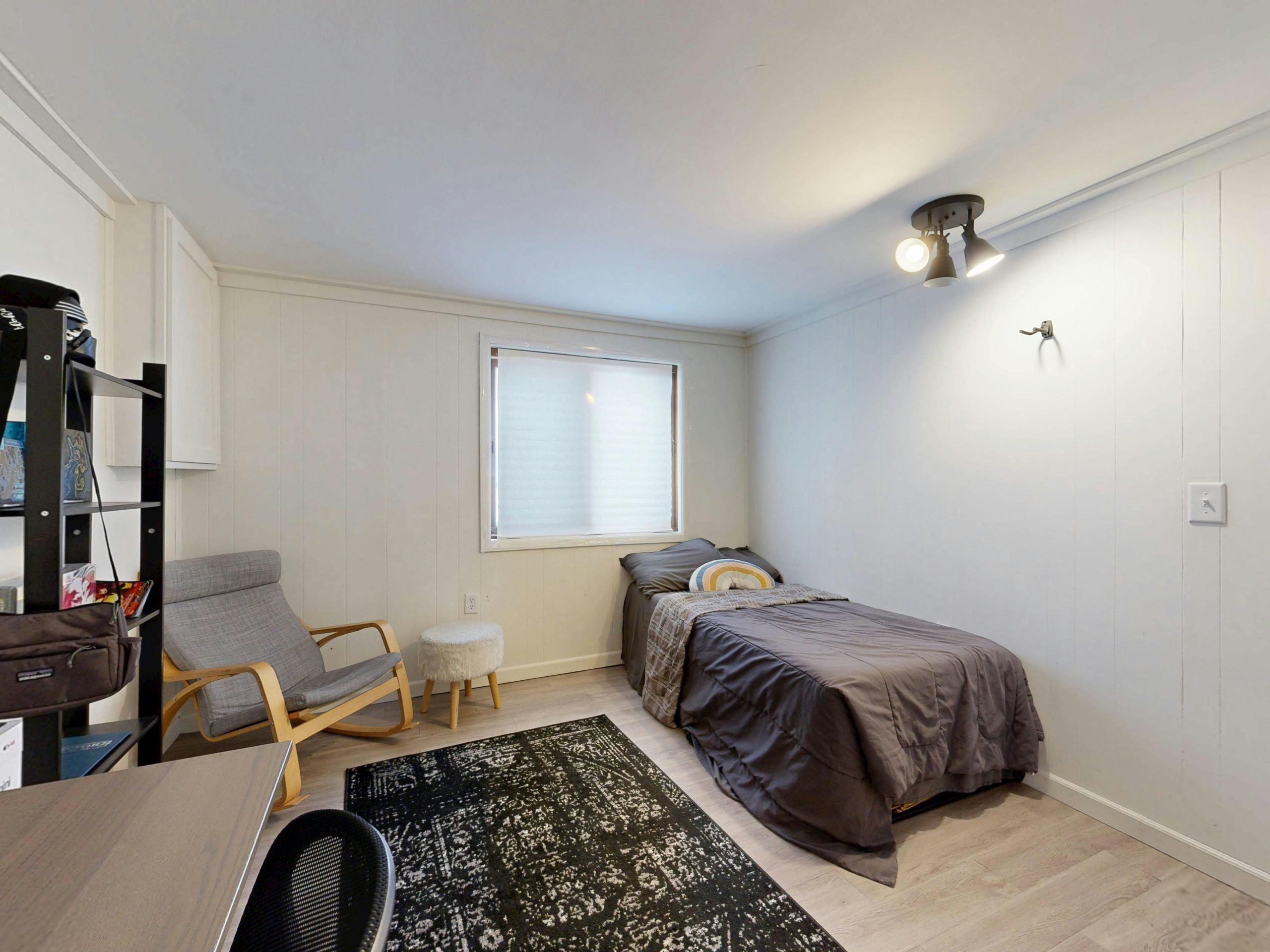 A simple minimalist bedroom with a grey bedspread, armchair, and modern decor. Une chambre minimaliste simple avec un couvre-lit gris, un fauteuil et une décoration moderne.
