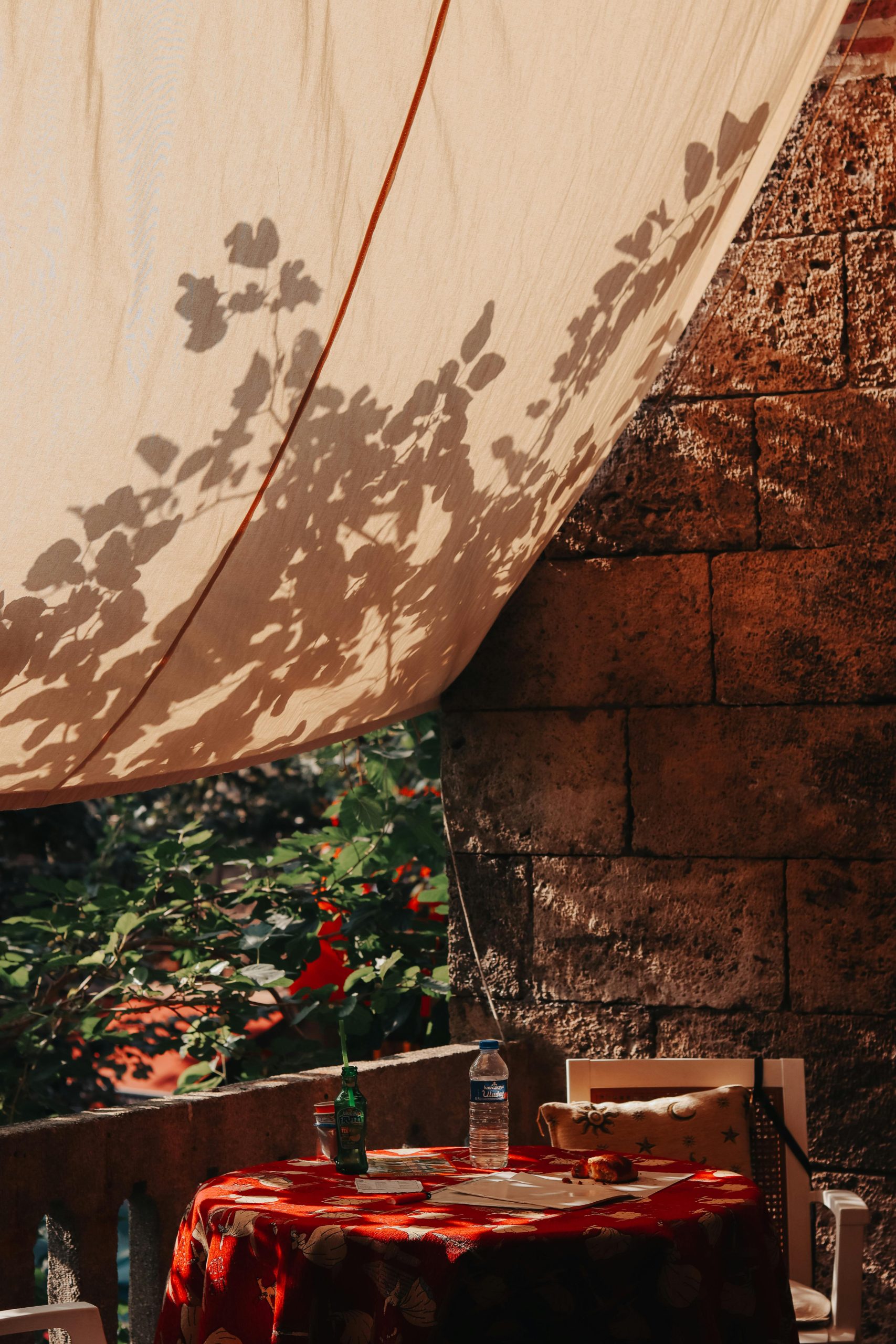 Terrasse extérieure relaxante avec un auvent en tissu ensoleillé projetant des ombres de feuilles, parfait pour les après-midis d'été.