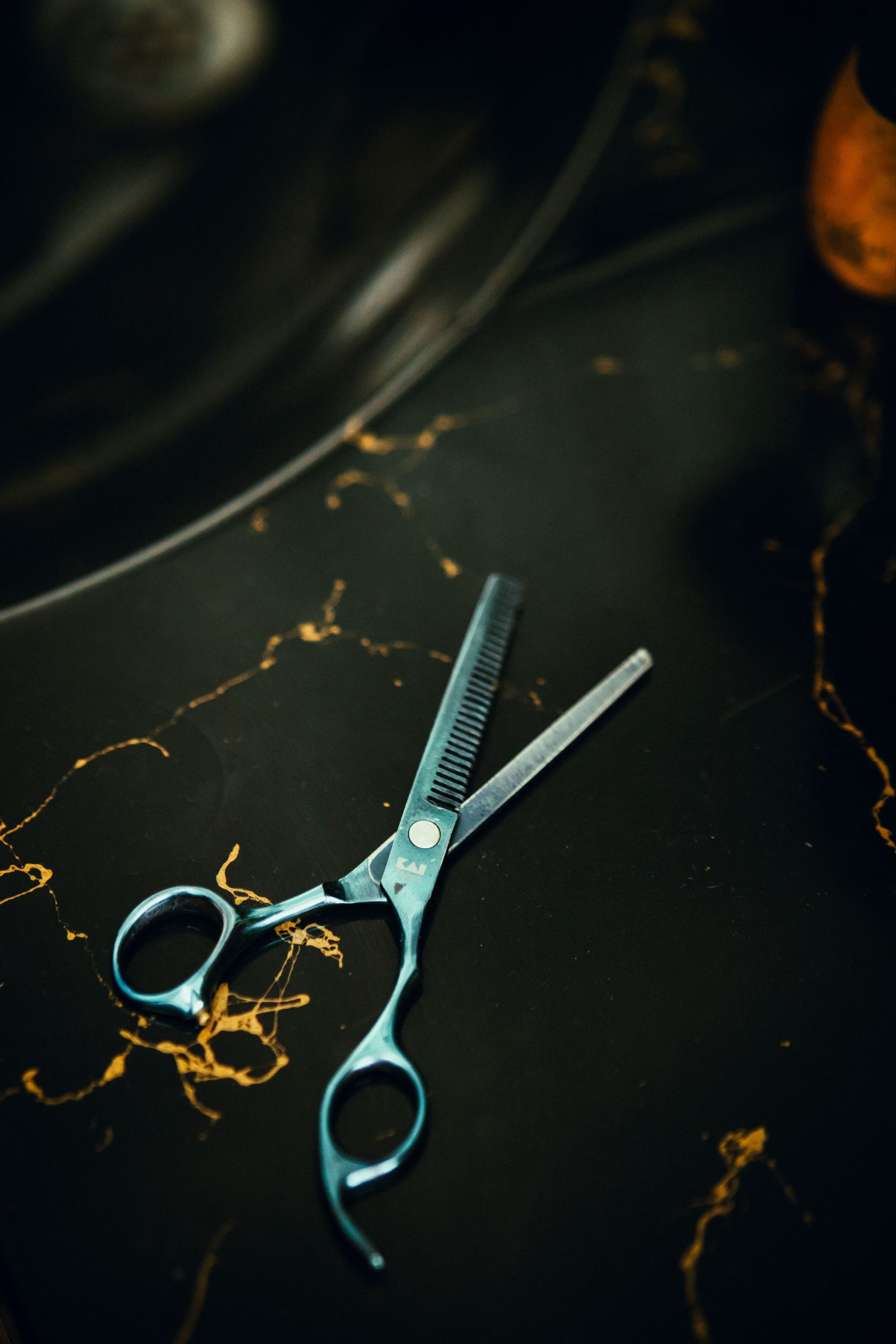 Close-up of professional hair thinning shears on a dark marble surface, perfect for hair styling and salon themes. Gros plan de ciseaux professionnels à effiler les cheveux sur une surface de marbre noir, parfait pour les thèmes de coiffure et de salon.