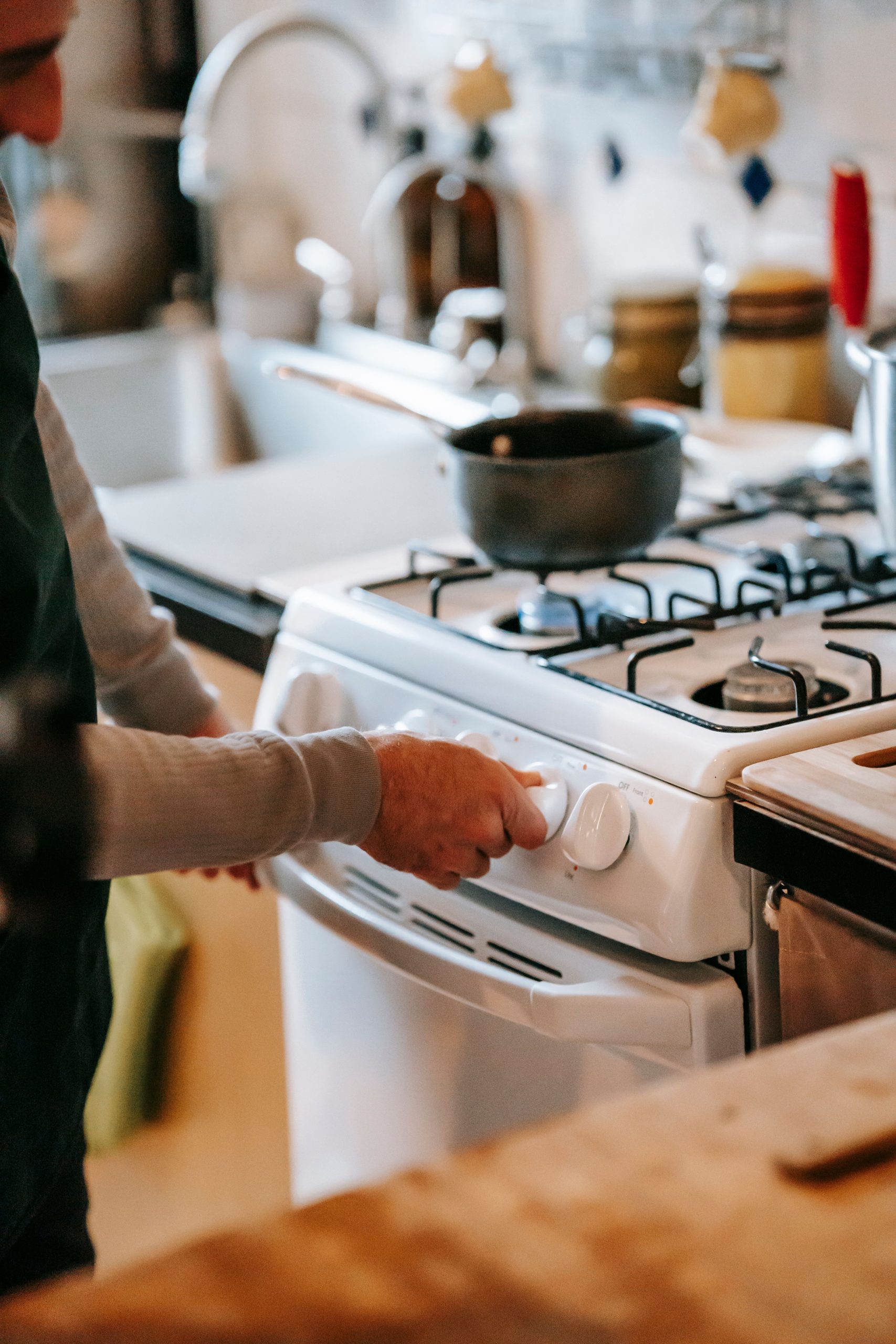 Crop anonymous male in casual clothes using gas stove with pan near counter and sink with tap near utensil in light kitchen at home Un homme anonyme en vêtements décontractés utilisant une cuisinière à gaz avec une poêle près du comptoir et de l'évier avec un robinet près des ustensiles dans une cuisine lumineuse à la maison