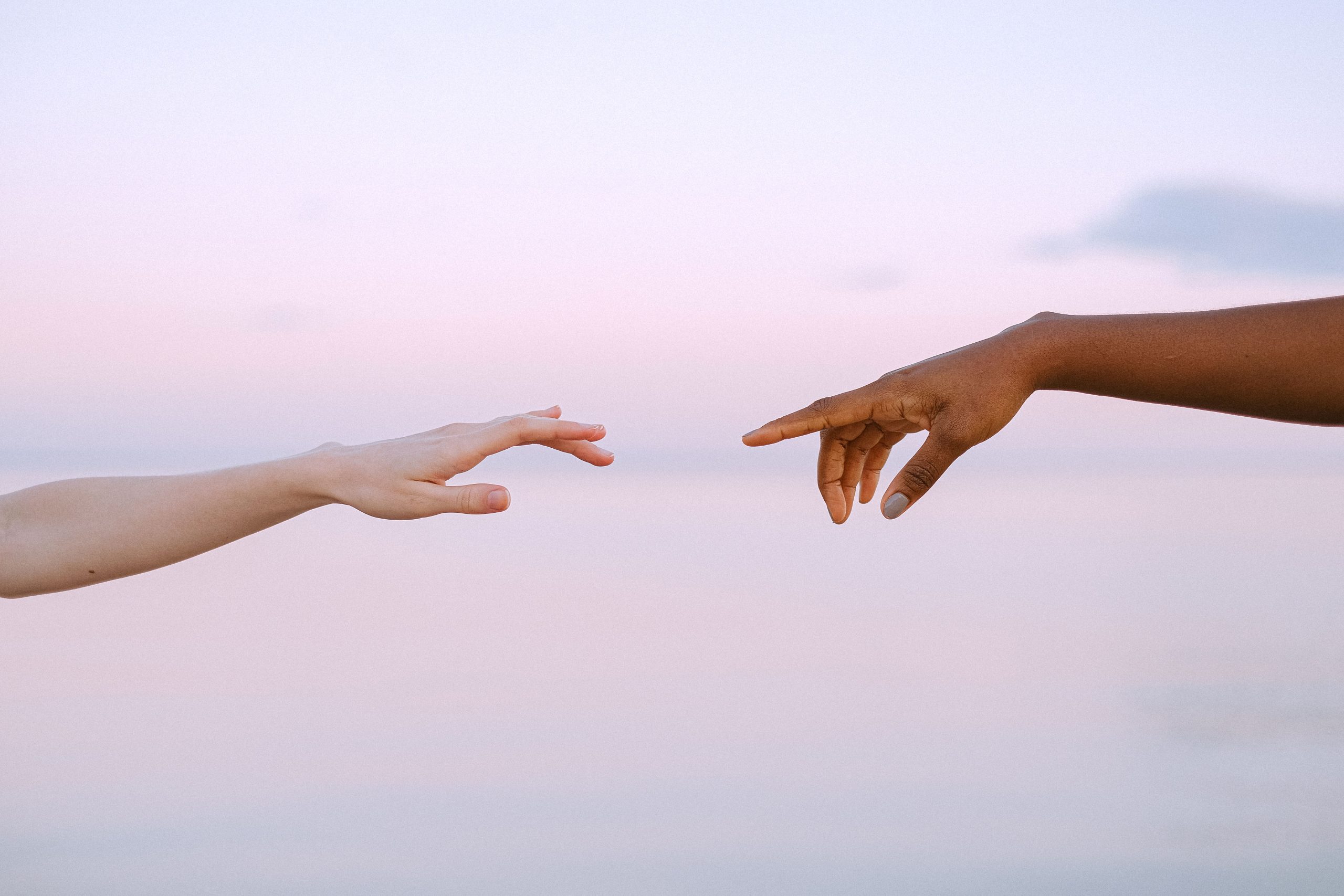 Two diverse hands reaching out across a pastel horizon, symbolizing unity and connection. Deux mains diverses se tendant à travers un horizon pastel, symbolisant l'unité et la connexion.