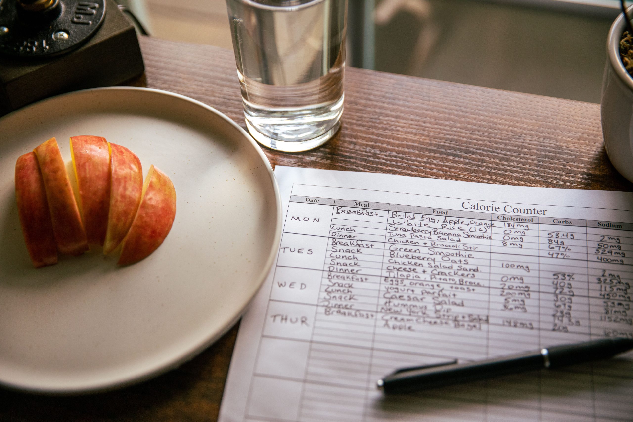 A table setup with apple slices, a calorie counting sheet, and a glass of water for a dieting scene. Une table dressée avec des tranches de pomme, une feuille de comptage des calories et un verre d'eau pour une scène de régime.