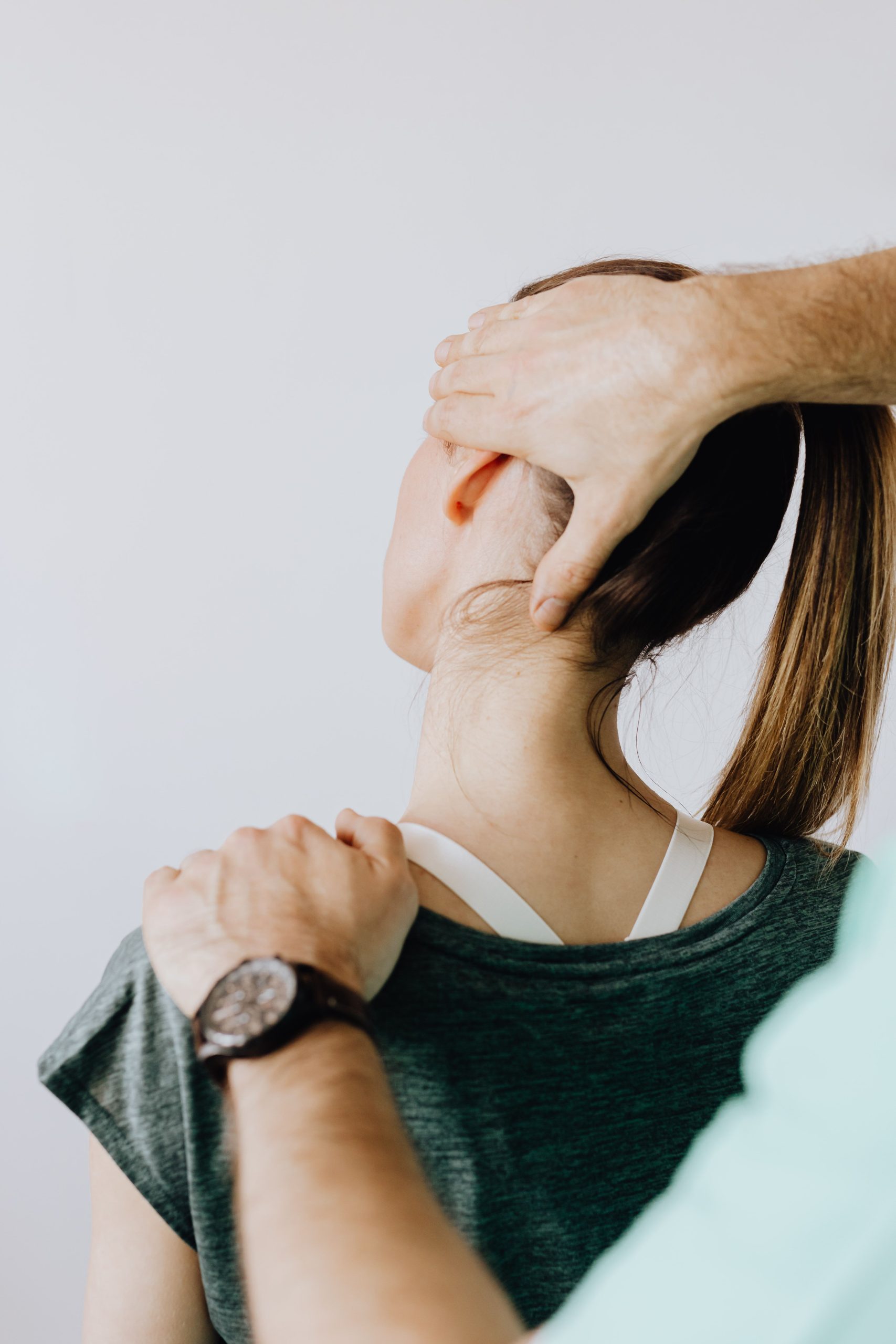 Back view of crop faceless chiropractor in wristwatch stretching neck of unrecognizable female patient during medical examination in doctor office in clinic Vue arrière d'un chiropraticien sans visage portant une montre étirant le cou d'une patiente méconnaissable lors d'un examen médical au cabinet du médecin à la clinique