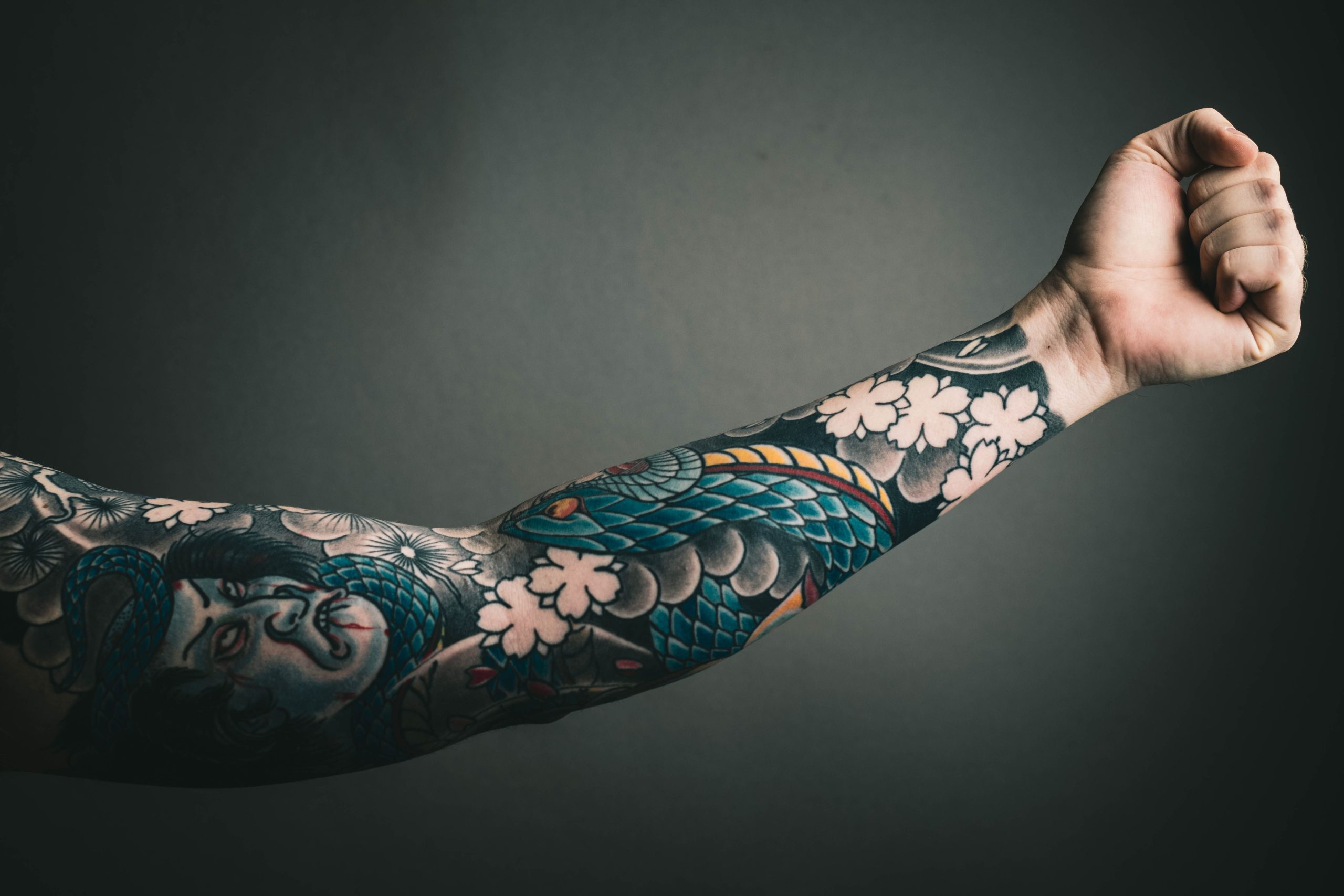 A close-up of a tattooed arm with a colorful sleeve design, featuring floral and artistic elements. Gros plan d'un bras tatoué avec un design de manche coloré, présentant des éléments floraux et artistiques.