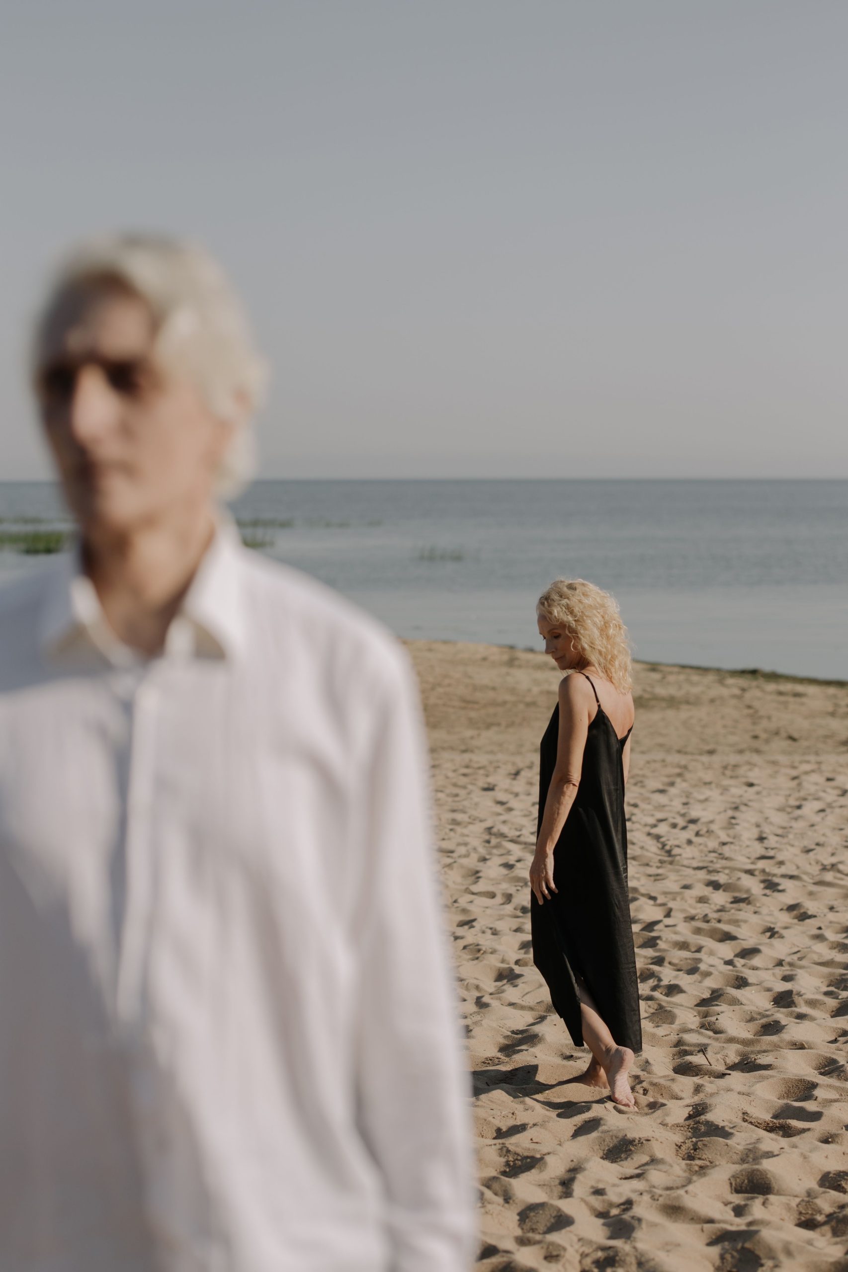 An elder couple stands on a tranquil beach, capturing a serene moment by the sea. Un couple de personnes âgées se tient sur une plage tranquille, capturant un moment serein au bord de la mer.