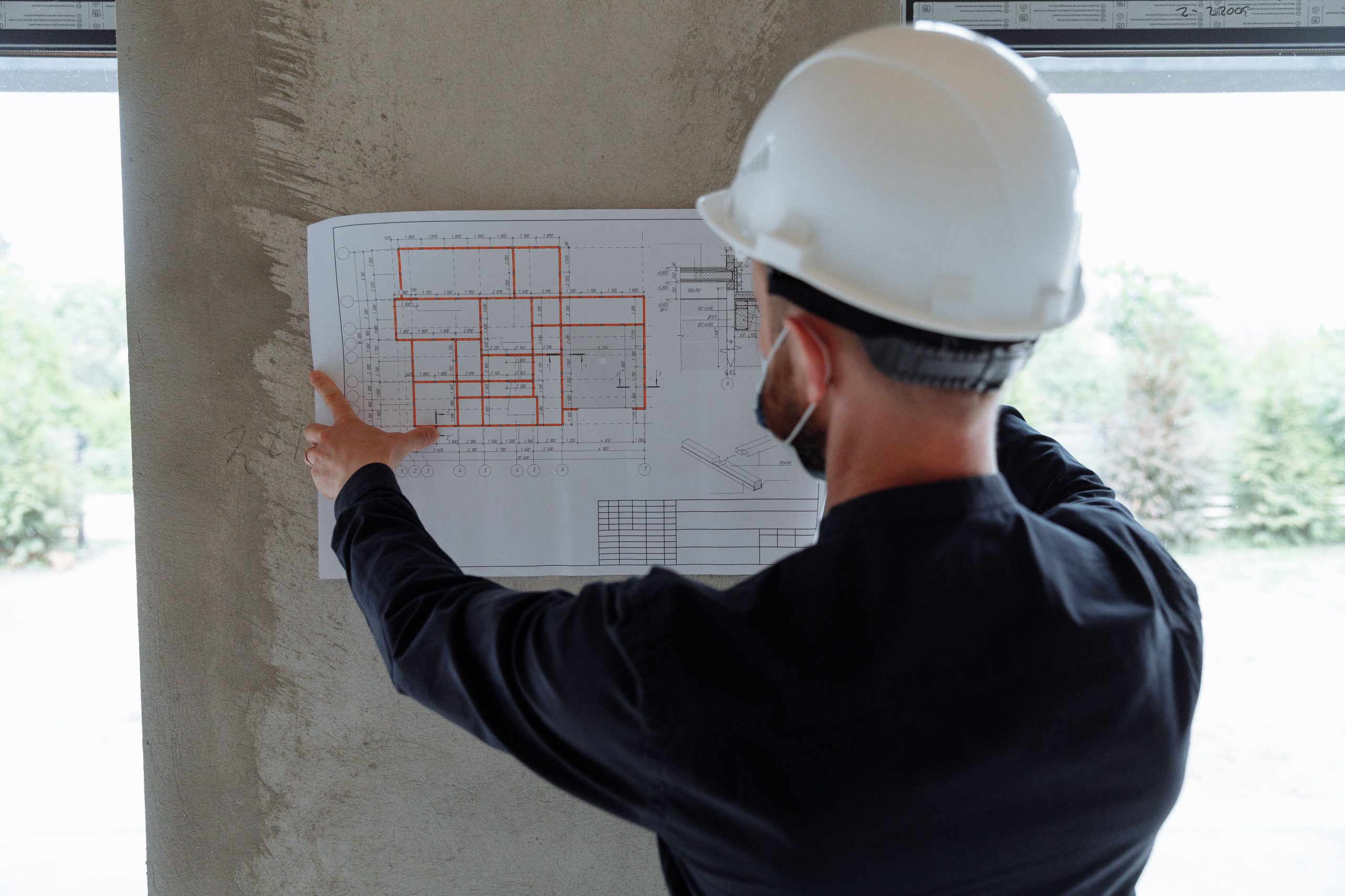 Engineer in hardhat reviewing architectural floor plans at construction site. Ingénieur au casque examinant des plans architecturaux sur un chantier de construction.